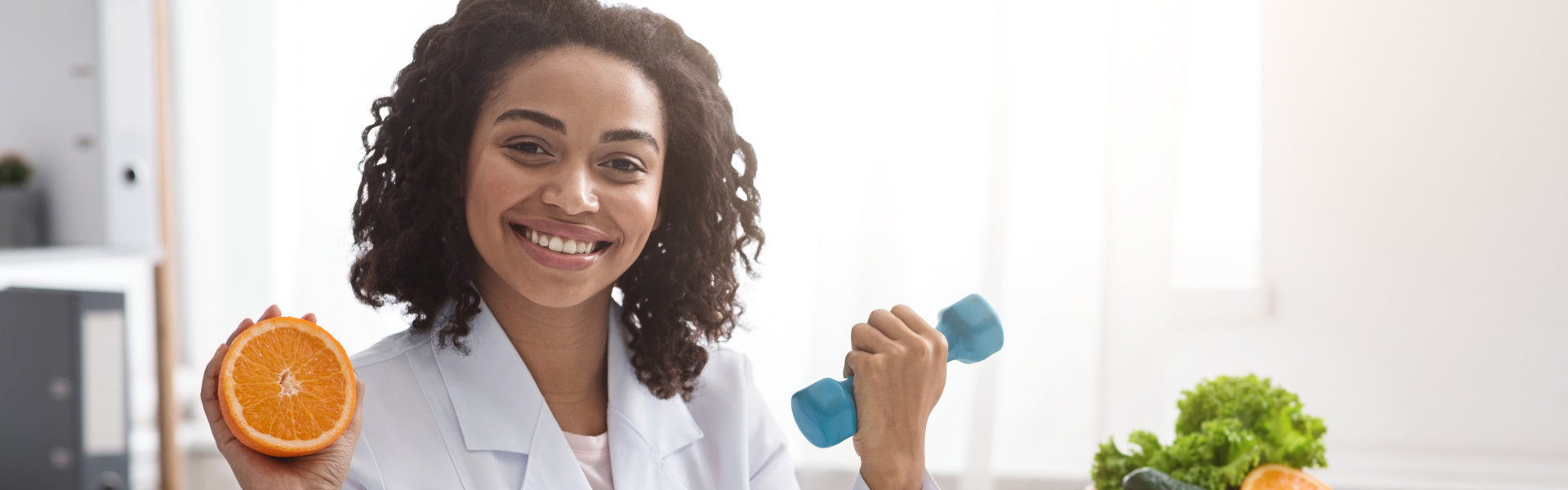 woman holding a dumbbell and a fruit smiling