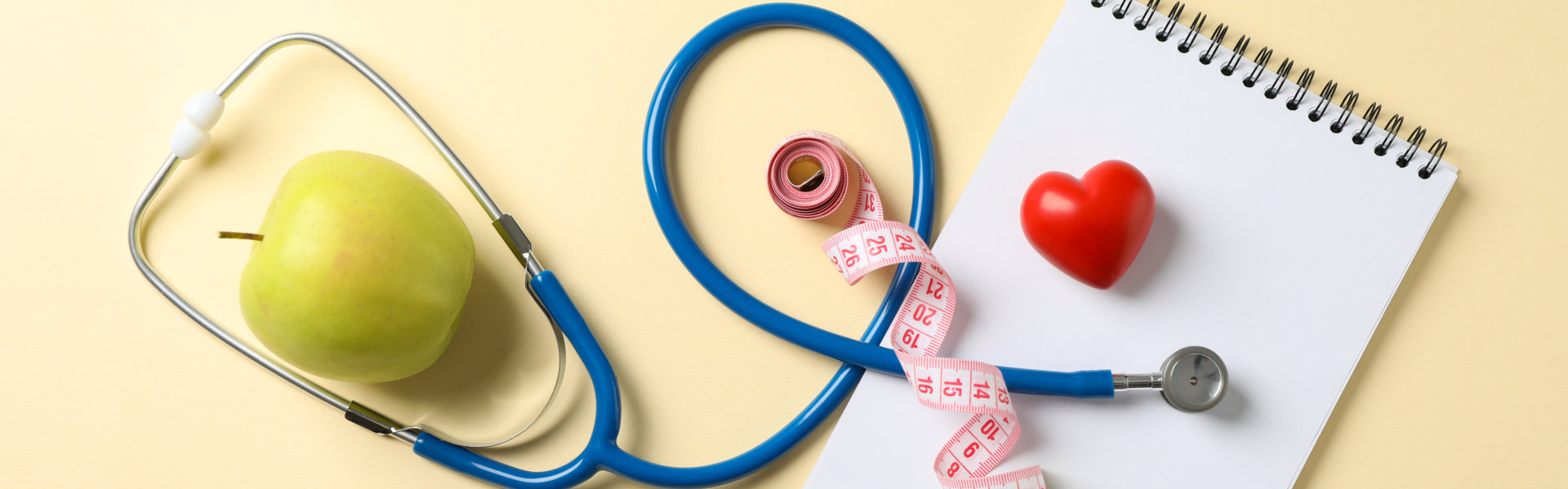 stethoscope, apple, notebook, heart and measuring tape on table